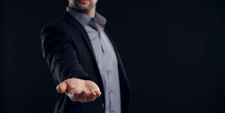 Businessman with outstretched hand on dark backgroundの写真素材