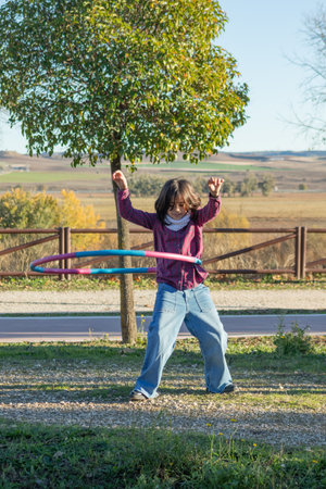 A young girl with short brown hair, wearing a pink shirt, is having a blast playing with a hula hoop in the park. She is full of energy, smiling, and clearly enjoying herself as she spins the hoop with excitement.の写真素材