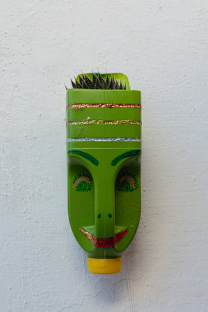 This intriguing and original photo features a handmade terracotta pot crafted from a reuse green glass bottle. The pot has been creatively painted with a face, giving it an eccentric and mysterious character. Above the face, plants grow as if sprouting from the top of their "head," resembling hair in a surreal and unique way.の写真素材