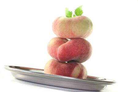 three fresh mountain peaches with lemon balm on a tray on a white backgroundの写真素材