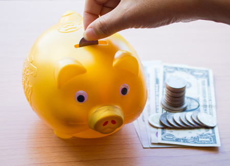 Inserting a coin into a piggy bankの写真素材