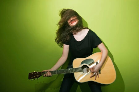 Portrait of a young woman playing the guitar and shaking her hair with green background.の写真素材