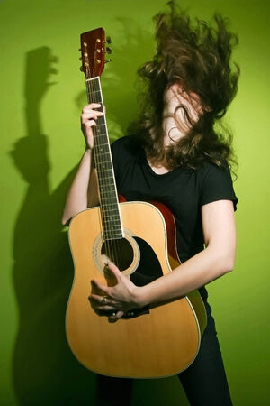 Portrait of a young woman playing the guitar and shaking her hair with green background.の写真素材