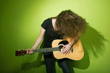 Portrait of a young woman shaking her hair and playing the guitar with green background.の写真素材