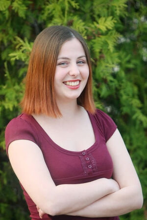 Young woman looking at the camera and posing outdoors in front of a pine tree.