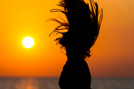 Silhouette of a woman waving her hair at sunset の写真素材