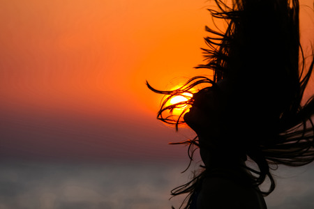 Silhouette of a woman tossing hair at sunset の写真素材