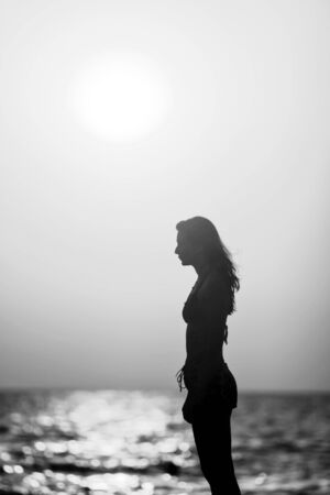 Silhouette of a woman standing on the beach at sunset の写真素材