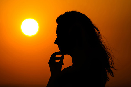 Silhouette of a woman touching her chin with her hand at sunset の写真素材