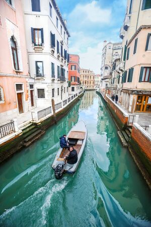 VENICE, ITALY - FEBRUARY 15 : A view of a boat with two man sailing in the water canal with people walking in the street on February 15th, 2014 in Venice, Italy.のeditorial素材