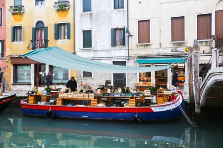 VENICE, ITALY - FEBRUARY 15 : Fruit and vegetable market place on a boat in a water canal with people walking in the street on February 15th, 2014 in Venice, Italy.のeditorial素材