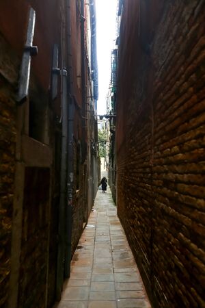 VENICE, ITALY - FEBRUARY 15 : A woman walking in the narrow street between buildings on both sides on February 15th, 2014 in Venice, Italy.のeditorial素材