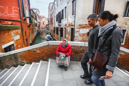 VENICE, ITALY - FEBRUARY 15 : A view of an older woman sitting on the bridge in the city and begging the passersby for money on February 15th, 2014 in Venice, Italy.のeditorial素材