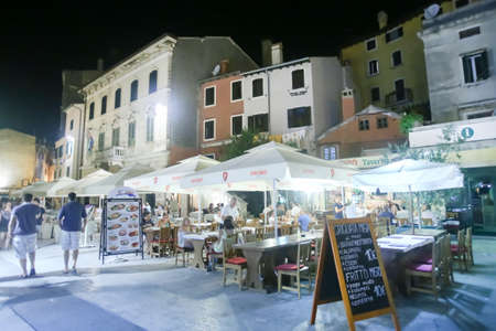 ROVINJ CROATIA  AUGUST 6 : Tourists walking in the street next to people sitting in a restaurant at night on August 6th 2013 in Rovinj Croatia. Rovinj is a tourist destination on Adriatic coast of Croatia.のeditorial素材