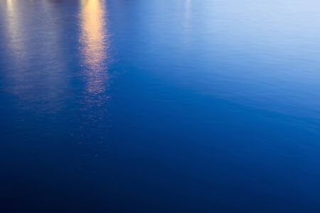 An abstract of the sea water surface at sunset with reflection of street light.の写真素材