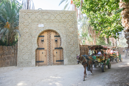 TUNIS, TUNISIA - SEPTEMBER 16, 2012 : Carriages with tourists passing by a door to the oasis in Tozeur, Tunisia.のeditorial素材