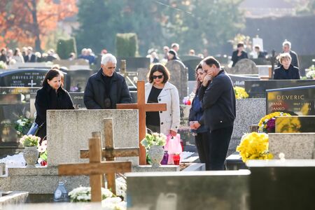 VELIKA GORICA, CROATIA - NOVEMBER 1, 2016 : People praying in front of graves decorated with floral...