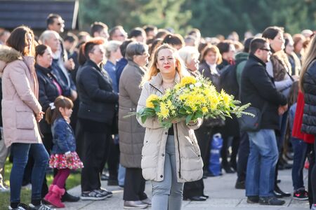 VELIKA GORICA, CROATIA - NOVEMBER 1, 2016 : A front view of a woman carrying a floral arrangement with people praying at a mass in the background at cemetery on All Saints day in Velika Gorica, Croatia.のeditorial素材