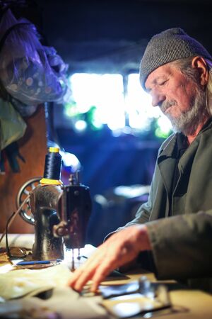 A senior adult man sewing a piece of cloth on a sewing machine.