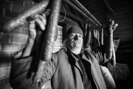 An old man posing with dry sausages hanging in the attick.の写真素材