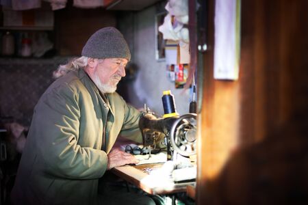 A senior adult man sewing a piece of cloth on a sewing machine.の写真素材