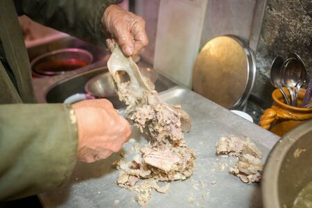 A man removing pork meat from the bone with a fork.