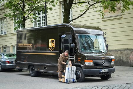 MUNICH, GERMANY - MAY 9, 2017 : An UPS worker putting packages on mobile trolley in the street in Munich, Germany.のeditorial素材