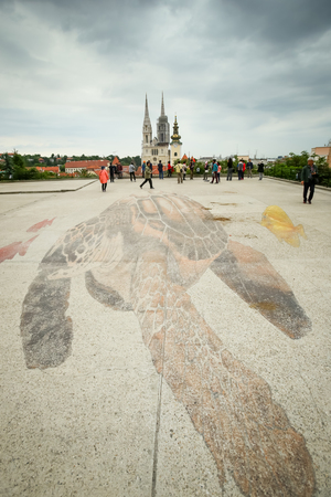 ZAGREB, CROATIA - MAY 20, 2017 : People sightseeing the 3D giant turtle painted on the floor of the plateau Gradec within the White night festival with a view of the Zagreb Cathedral in the background in Zagreb, Croatia.のeditorial素材