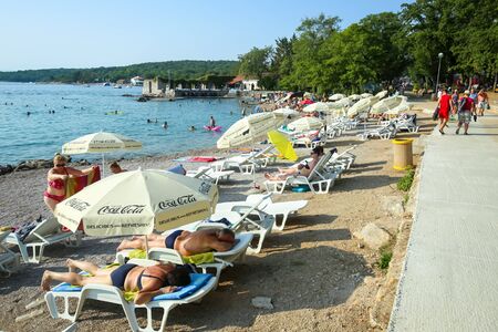 NJIVICE, CROATIA - JUNE 24, 2017 : People relaxing on deck chairs under parasols and swimming in the Adriatic sea in Njivice, Croatia.のeditorial素材