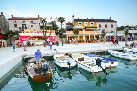 NJIVICE, CROATIA - JUNE 24, 2017 : Anchored boats lined up with people at the seafront full of shops and restaurants at sunset in Njivice, island of Krk, Croatia.のeditorial素材