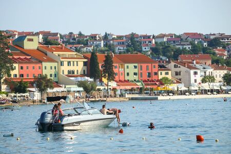 NJIVICE, CROATIA - JUNE 24, 2017 : People on the anchored boat with colorful architecture of hotel Jadran in the background in Njivice, island Krk, Croatia.のeditorial素材
