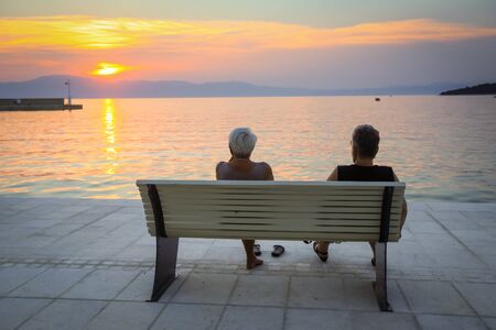 Two senior women enjoying the sunset on the bench at the waterfront in Njivice,  island Krk, Croatia.の写真素材