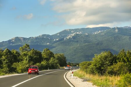 GRACAC, CROATIA - JULY 16, 2017 : Cars driving on a road through the rural landscape under cloudy sky in Gracac, Croatia.のeditorial素材