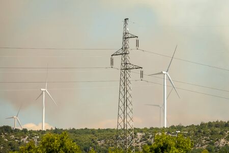 Power line with windmills in a smoke cloud from a forest fire in Dalmatia, Croatia.