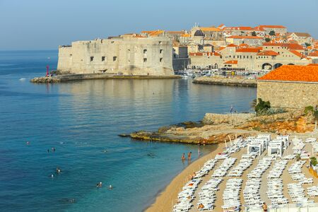 DUBROVNIK, CROATIA - JULY 22, 2017 : People bathing and sunbathing on the Banje beach with the city tower and walls in the background in Dubrovnik, Croatia.のeditorial素材