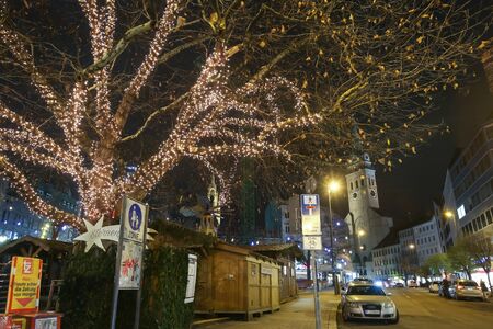 MUNICH, GERMANY - DECEMBER 11, 2017 : Illuminated ornated trees on the street with Saint Peters Church at the background at night in center of Munich, Germany.のeditorial素材