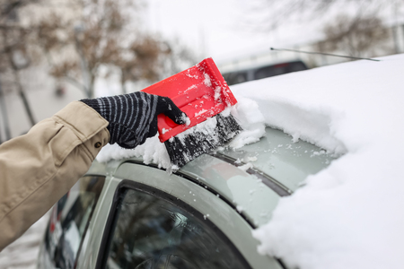 A woman cleaning the snow off the car roof in winter time.