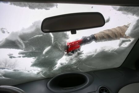 A woman cleaning the snow off the windshield viewed from the inside of the car.の写真素材