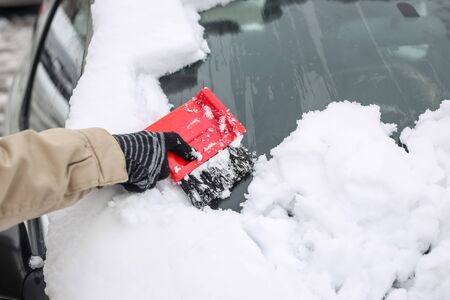 A woman cleaning the snow off the car in winter time.