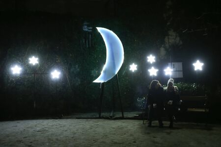 ZAGREB, CROATIA - DECEMBER 13th, 2017: Advent time in city center of Zagreb, Croatia. Two women sitting on the bench next to the illuminating moon and stars in the upper old town Gradec.のeditorial素材