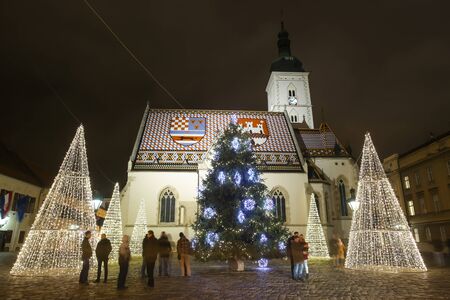 ZAGREB, CROATIA - DECEMBER 13th, 2017: People sightseeing the illuminated Christmas trees in front of the Saint Marks Church at St. Marks Square in the upper old town Gradec during Advent time.のeditorial素材