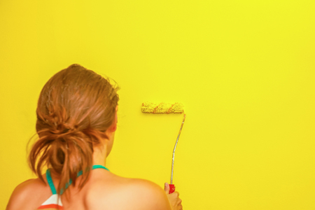 Female painting wall in yellow with paint roller.の写真素材