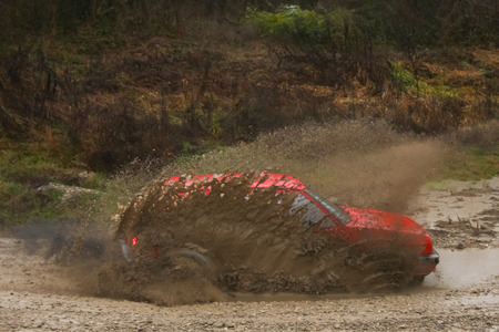 Red rally car driving thru the mud during the race