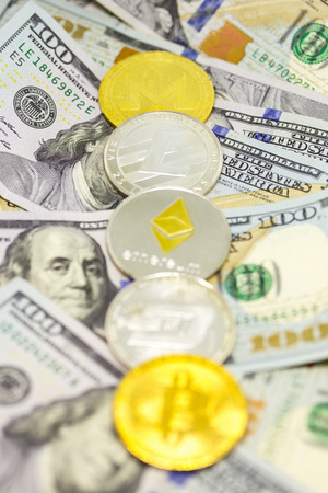 Lined up cryptocurrency coins displayed on a heap of one hundred dollar bills with focus on litecoin coin.の写真素材