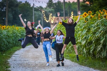Brezje, Croatia - 20th July, 2019 : Four young girls joyfully jumping on the pathway leading thru the field of sunflowers on the Forestland, ultimate forest electronic music festival.のeditorial素材
