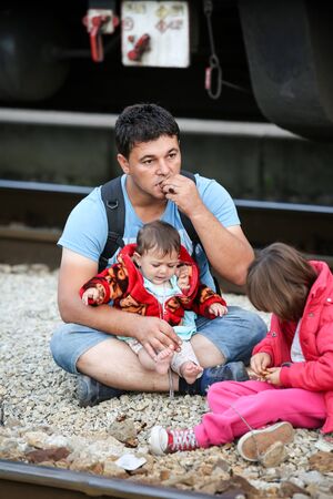 Dugo Selo,Croatia - September 17,2015: Syrian refugee man with children sitting on the train tracks after arriving from Serbia and waiting for the buses to continue to the northern european countries.のeditorial素材