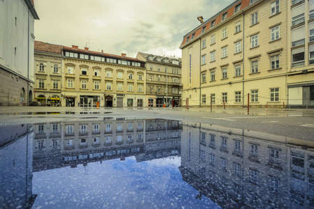 Zagreb, Croatia - April 16, 2020 : Reflection of the buildings in a puddle on the street after the...