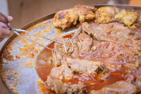 Detail of a human hand turning a pork steak meat cooked in vegetable sauce together with sausages and chicken meat on a barbeque fire in a traditional croatian kotlovina dish.の写真素材