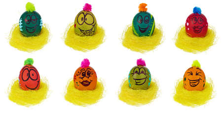 Easter egg, handmade painted in a smiling cartoon face, sit in a yellow bird's nest. Decorated eggs with funny colorful hairstyles and multi-colored patterns. Easter decorations on a white background with a light reflection.の写真素材