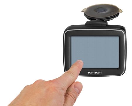 TomTom GPS car navigation with handle. The finger indicates the point on the satellite navigation screen. Black electronic map device with blue screen and silver border. Satellite navigation device isolated on white background.のeditorial素材